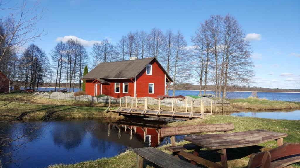 una casa roja con un muelle junto a un lago en Kempings Mežmalas en Usma