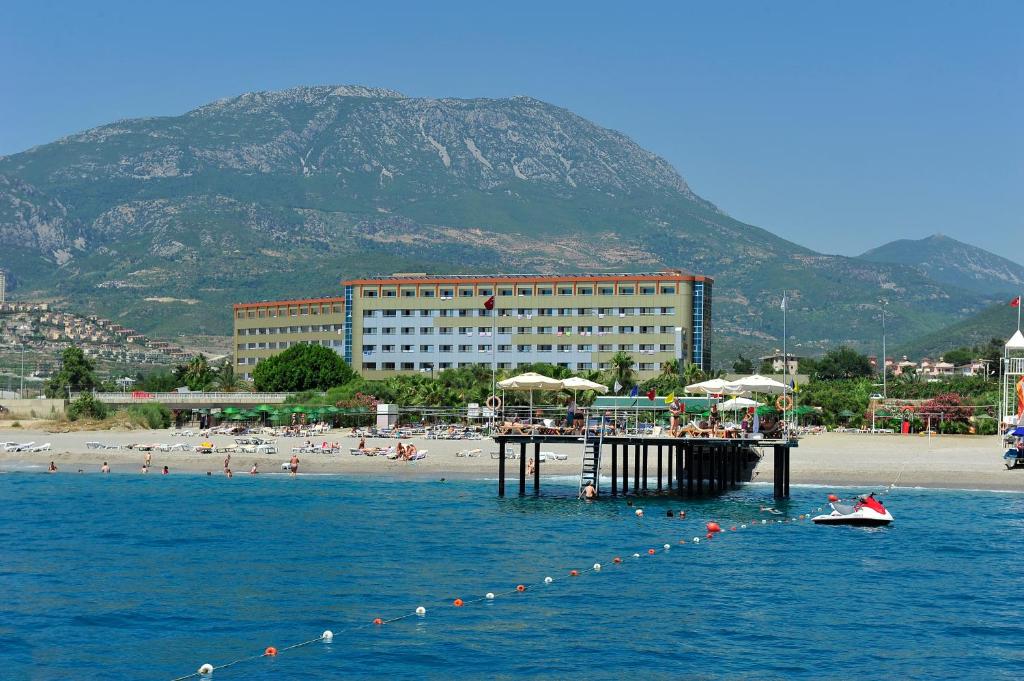 a pier in the water with a beach and a building at Kırbıyık Resort Hotel - Alanya in Kargicak