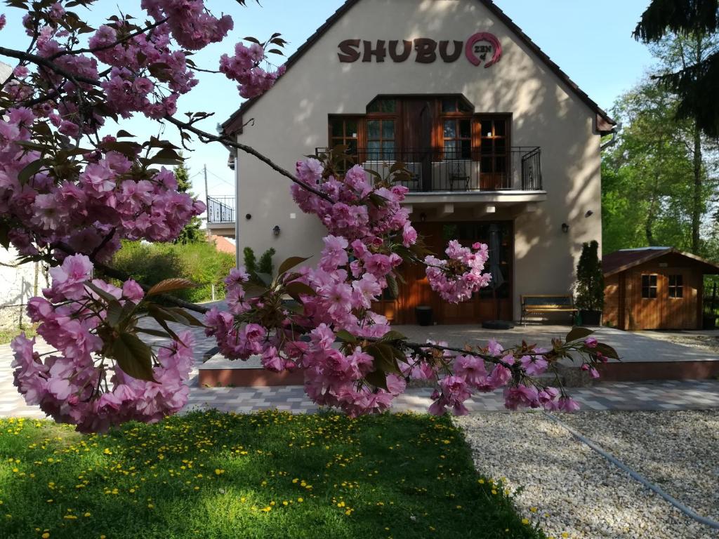 a building with a flowering tree in front of it at Shubu Zen Vendégház in Szilvásvárad