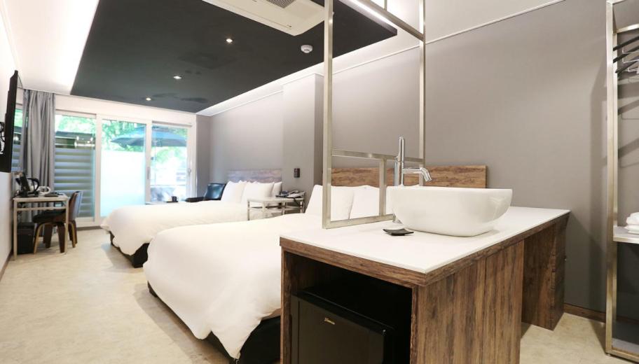 a bedroom with two beds and a sink and a mirror at Louis Hotel in Gangneung