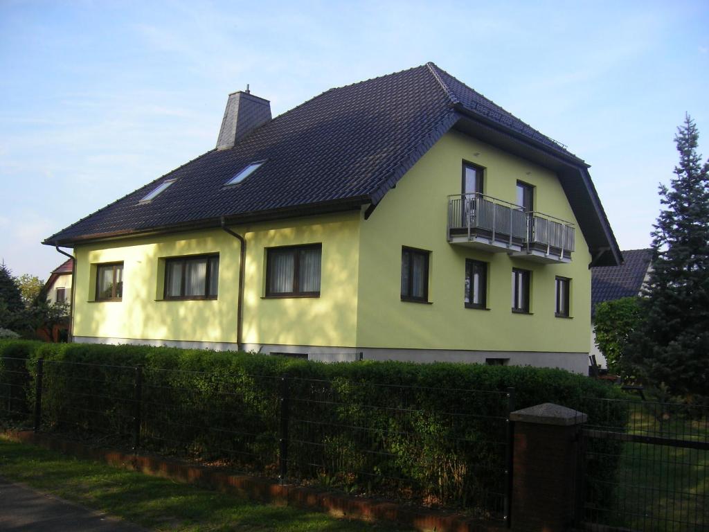 een geel huis met een zwart dak en een hek bij Spreewälder Ferienpension in Lübben