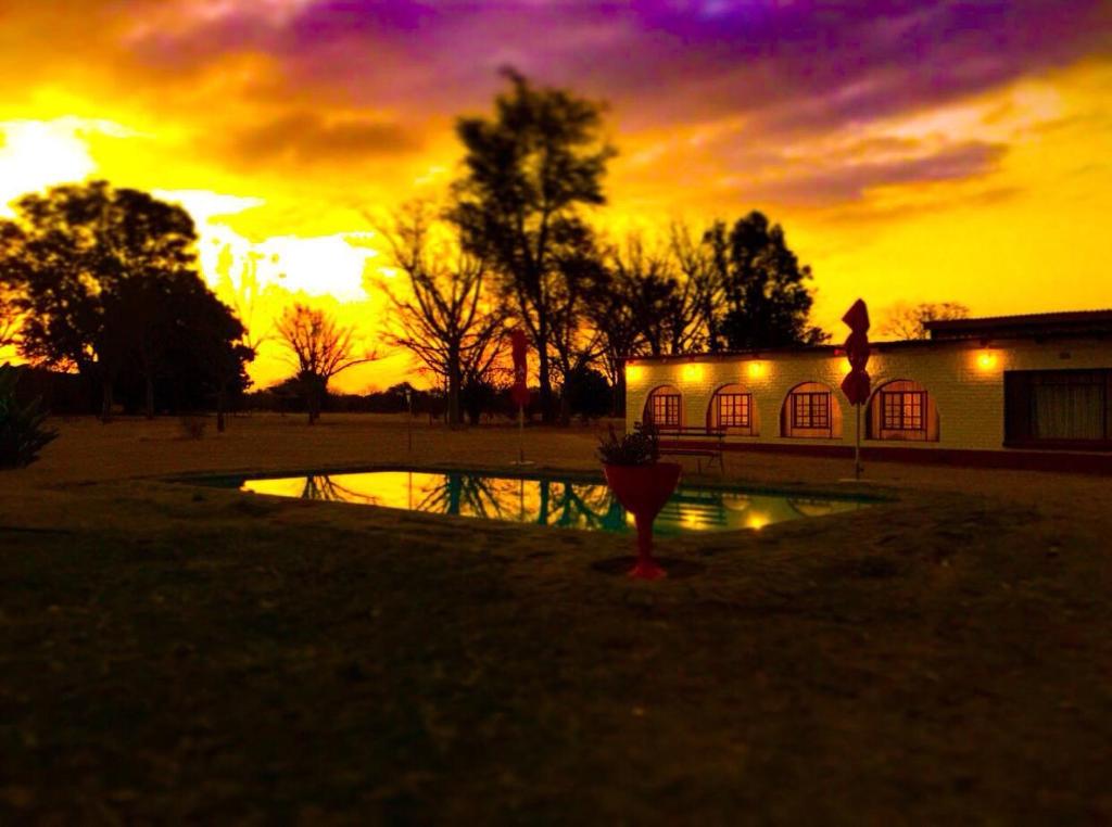 einen Sonnenuntergang mit einem Gebäude und einem Spiegelbild in einem Teich in der Unterkunft La Rive Waterberg Accommodation in Welgevonden Game Reserve