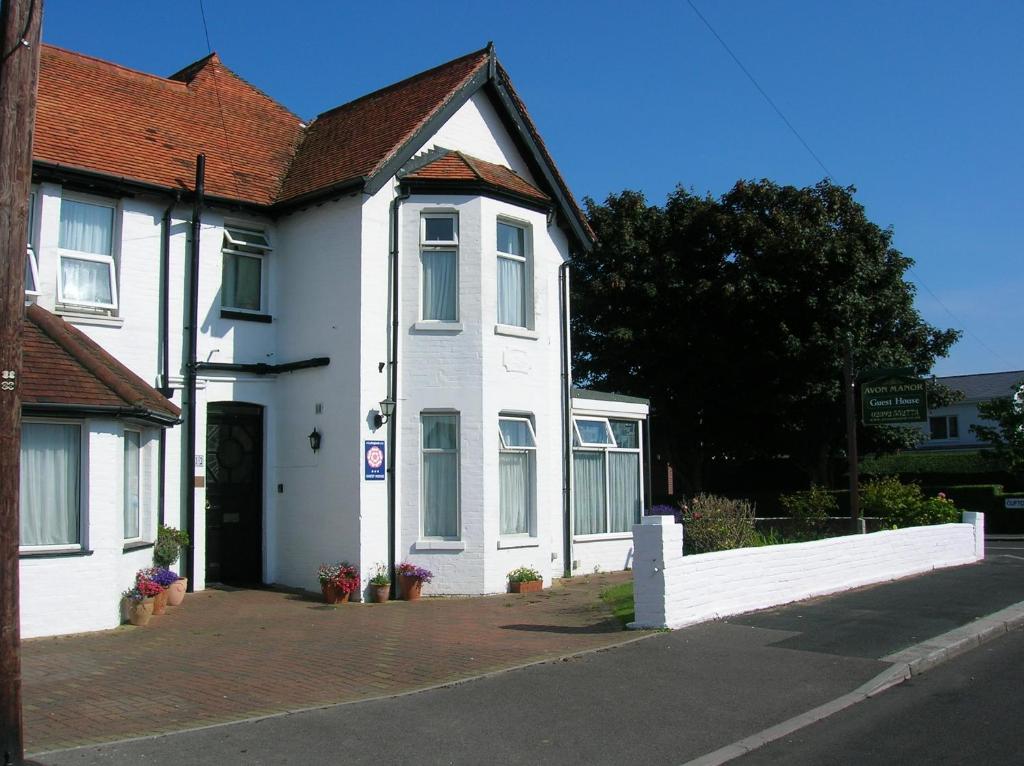 a white house with a red roof on a street at Avon Manor Guest House in Lee-on-the-Solent