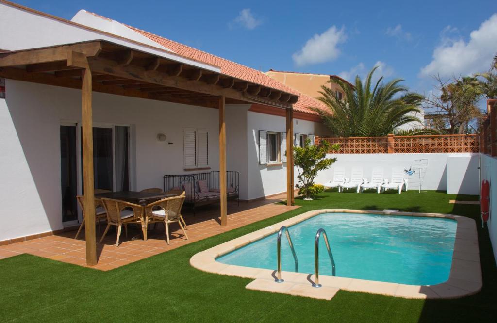 un patio trasero con piscina, mesa y sillas en Villa Taginaste en Corralejo