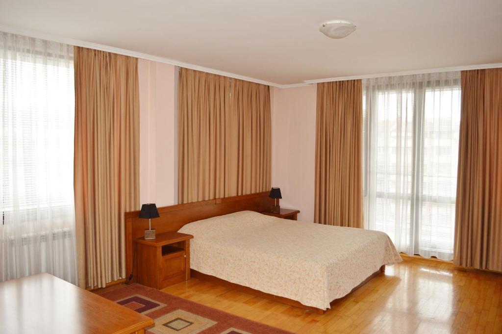 a bedroom with a bed and a table and windows at Hotel Drama Burgas in Burgas