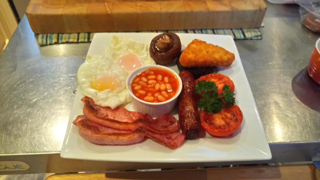 a plate of breakfast food with bacon eggs beans and toast at Camellia Lodge Guest House in Weston-super-Mare