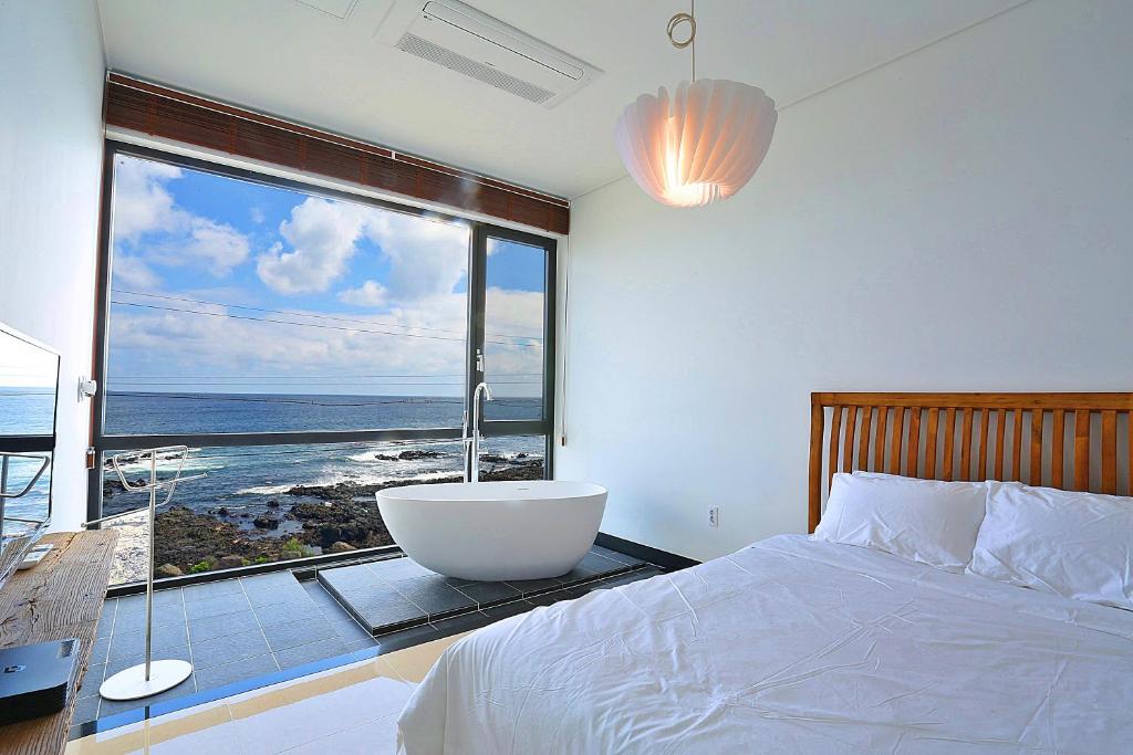 a bedroom with a large window with a bath tub at The Villas Ocean for Family in Seogwipo