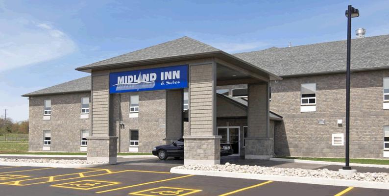 duży ceglany budynek z niebieskim znakiem na parkingu w obiekcie Midland Inn & Suites w mieście Midland