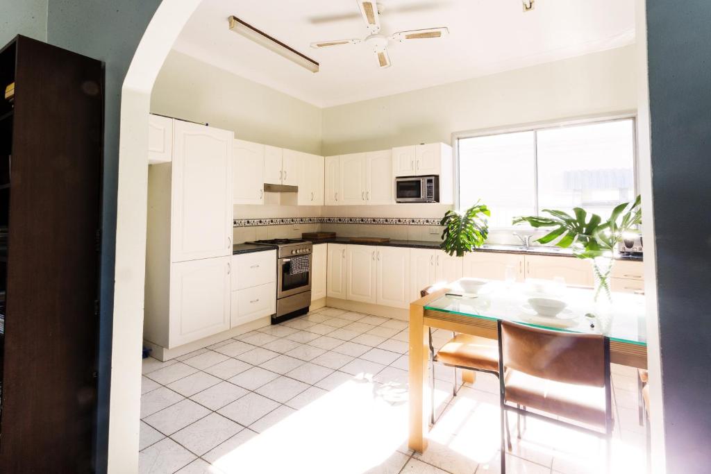 una cucina con mobili bianchi e un tavolo con sedie di Coal d' Vine Cottage - Cessnock NSW a Cessnock