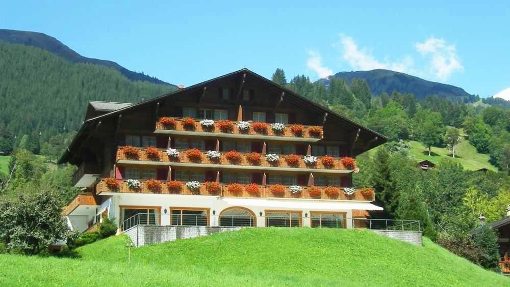 a large building on top of a green hill at Hotel Gletscherblick Grindelwald in Grindelwald