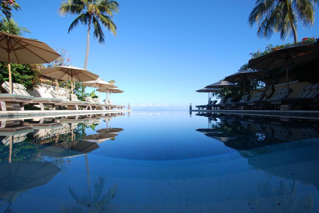 einen Pool mit Sonnenschirmen, Stühlen und Wasser in der Unterkunft Puri Mas Boutique Resort & Spa in Senggigi 