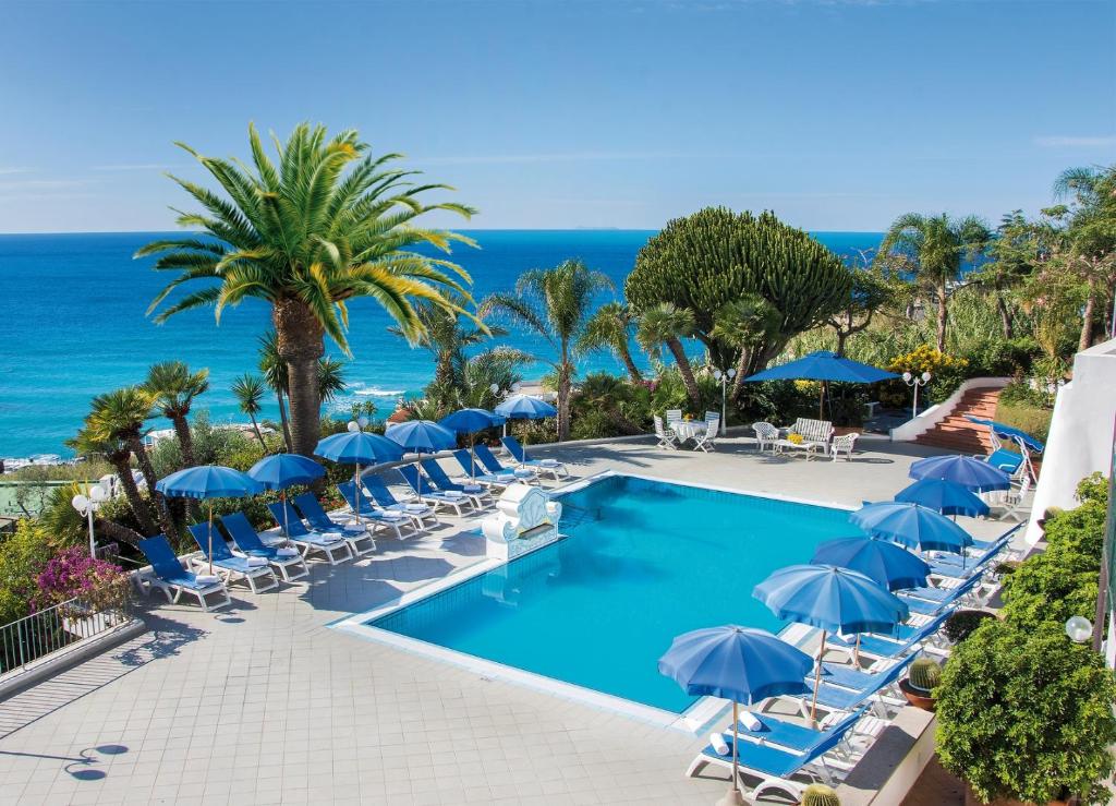a pool with chairs and umbrellas and the ocean at Hotel Capizzo in Ischia