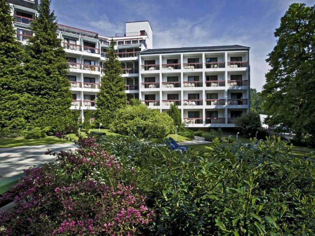 un grand immeuble d'appartements blanc avec des arbres et des fleurs dans l'établissement Hotel Lövér Sopron, à Sopron