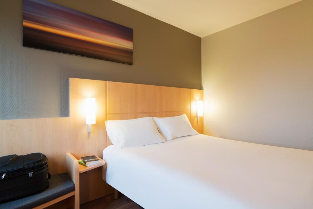 a hotel room with a bed and a suitcase on a table at ibis Rotterdam Vlaardingen in Vlaardingen