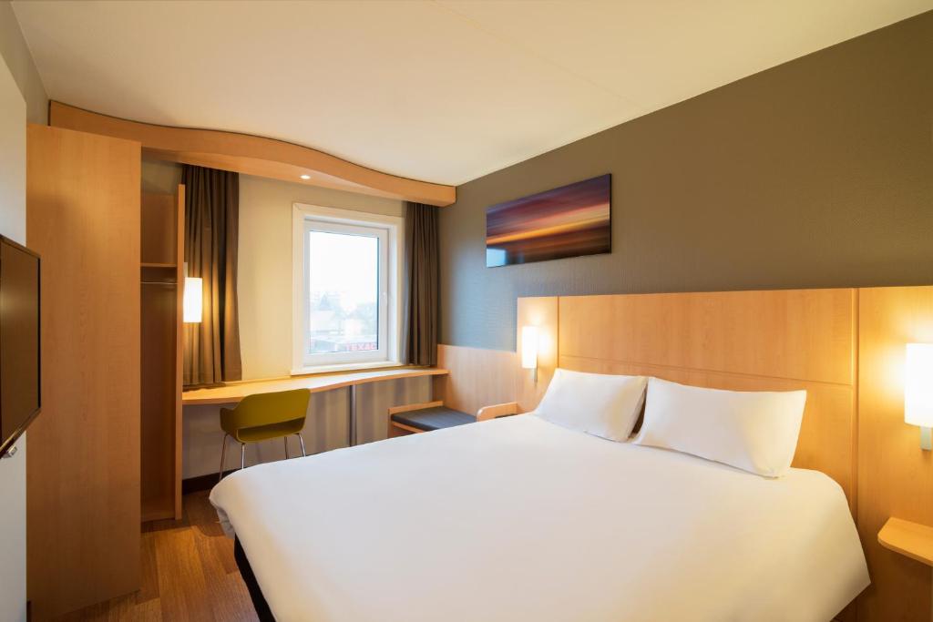 a hotel room with a large white bed and a window at ibis Rotterdam Vlaardingen in Vlaardingen