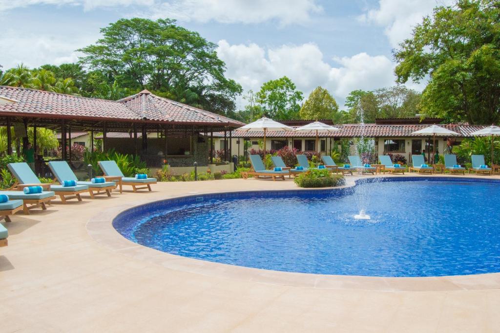 una piscina en un complejo con tumbonas azules en La Foresta Nature Resort en Quepos