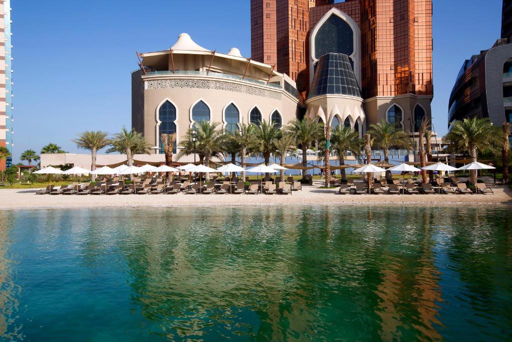 a building with chairs and umbrellas next to a body of water at Bab Al Qasr Residence in Abu Dhabi