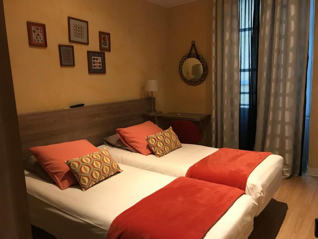 two beds in a hotel room with red and orange pillows at La Carpe d'Or in Fontainebleau