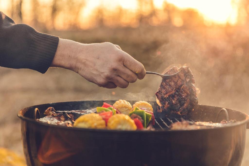 uma pessoa de mãos dadas com um garfo a cozinhar carne numa grelha em Bosgårdens Cottages em Broddetorp