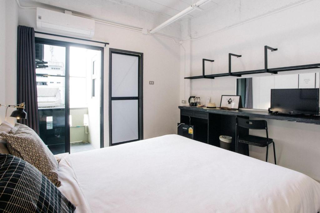 A bright bedroom with a large bed, wall-length desk, television and balcony door.