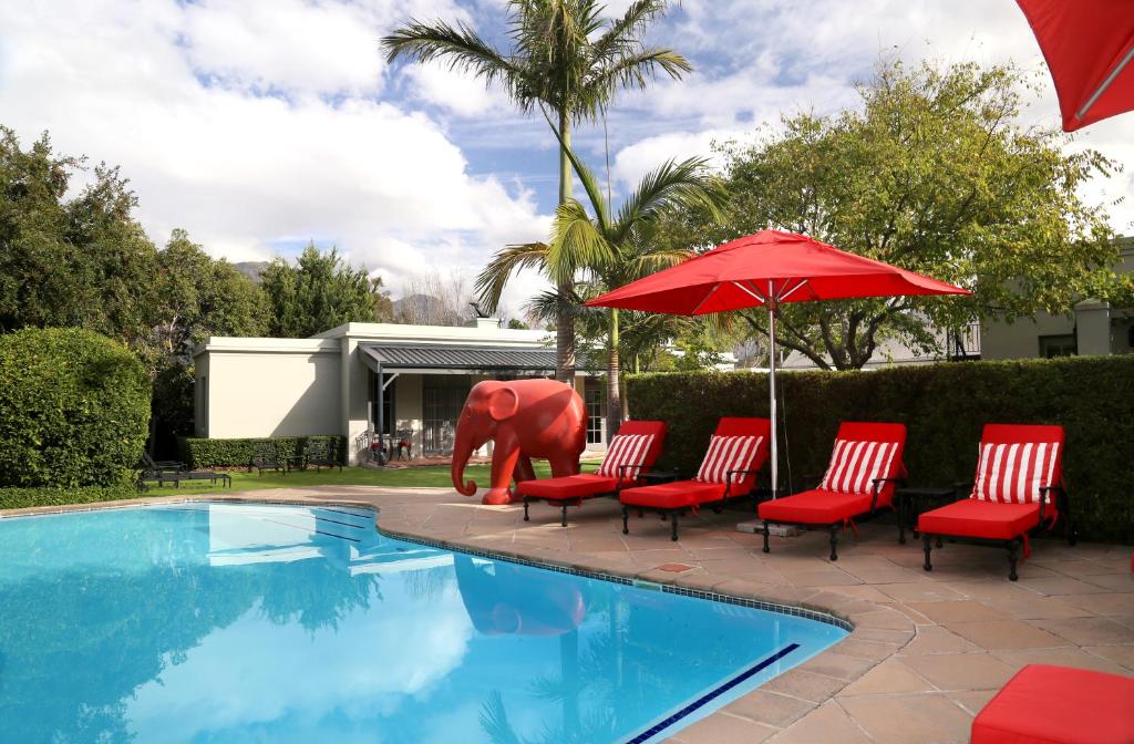 einem Pool mit Stühlen, einer Elefantenstatue und einem Regenschirm in der Unterkunft Avondrood Guest House by The Oyster Collection in Franschhoek