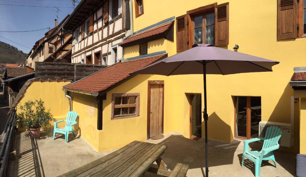 a yellow building with an umbrella and two chairs at Gîte Elisa et Léna in Riquewihr