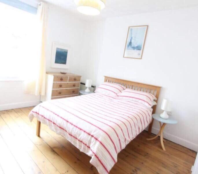a white bedroom with a bed with a striped blanket at Drang house all rooms have stairs in Padstow