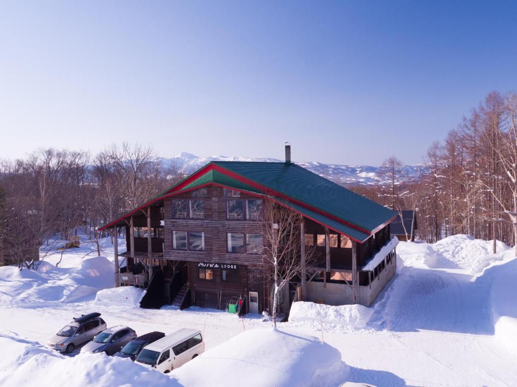 a log cabin in the snow with parked cars at Moiwa Lodge in Niseko