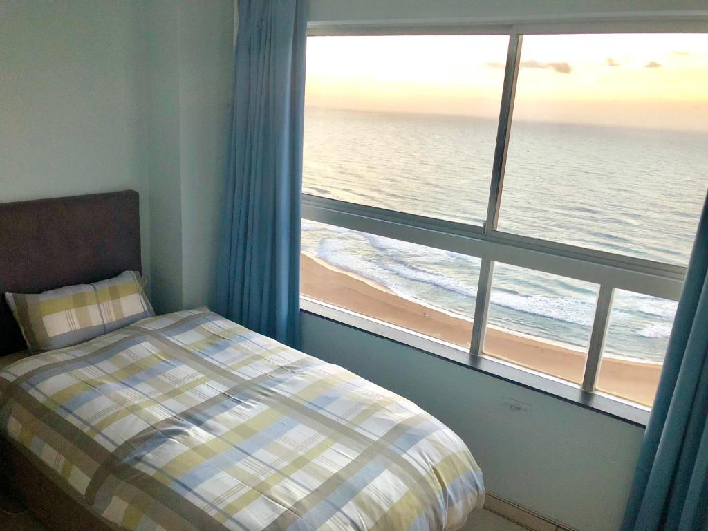 a bedroom with a window with a view of the ocean at Hightide Apartment in Amanzimtoti