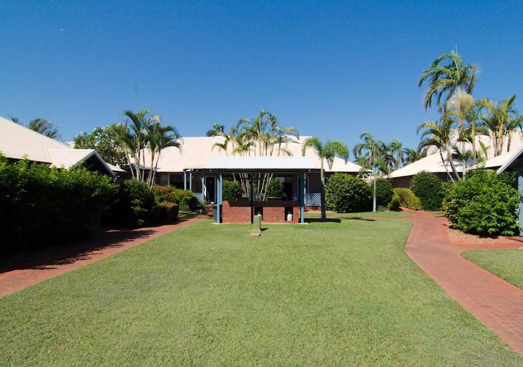 two people standing in a grassy area next to a tree at Cable Beach Apartments in Broome