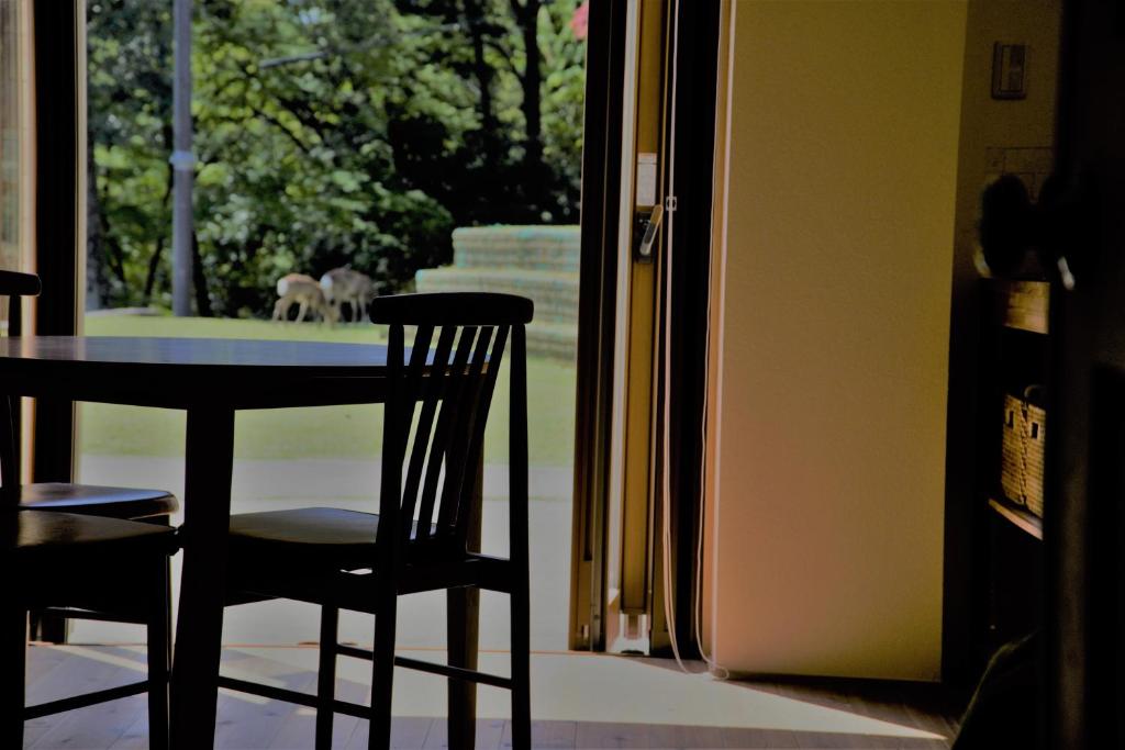 a dining room table with two chairs and a dog out the window at Mountain Home Lodge in Deer Park in Nara
