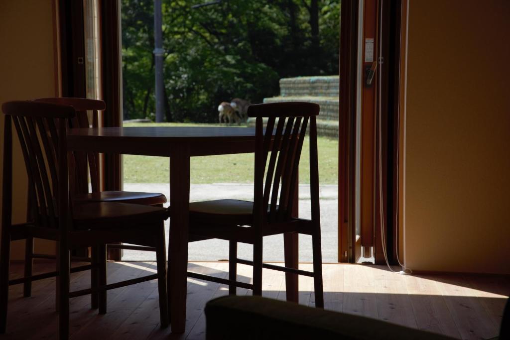 a table with two chairs and a dog looking out the window at Mountain Home Lodge in Deer Park in Nara