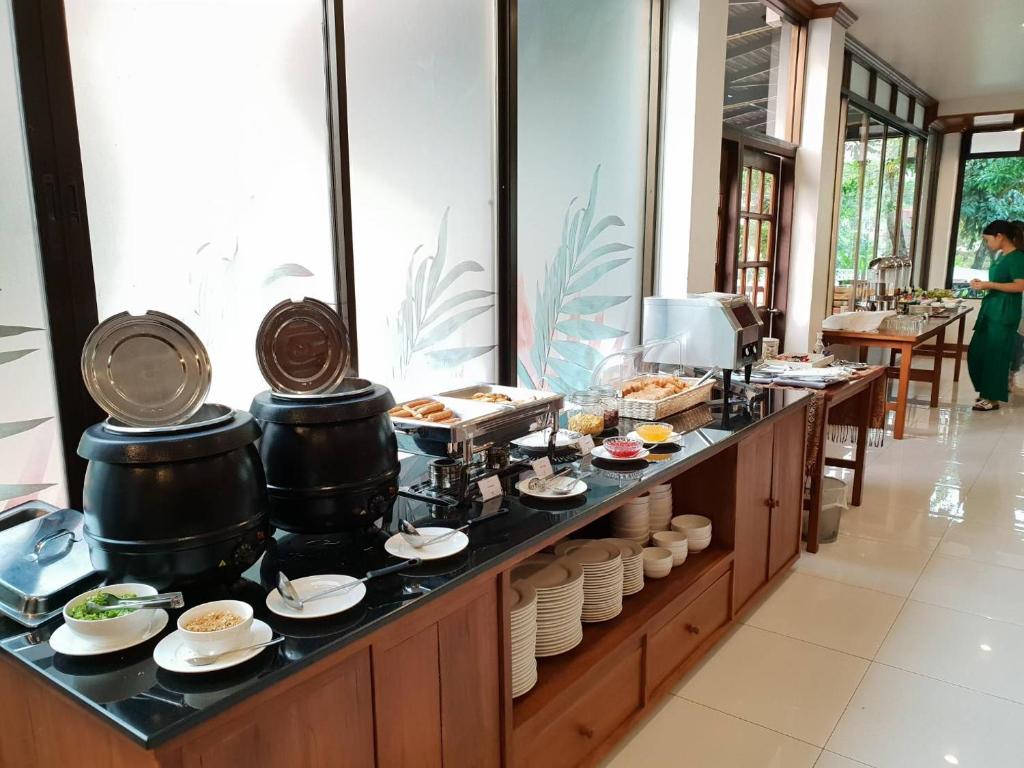 A long breakfast buffet line with soup pots, hot trays, toppings and stacked tableware by the windows.