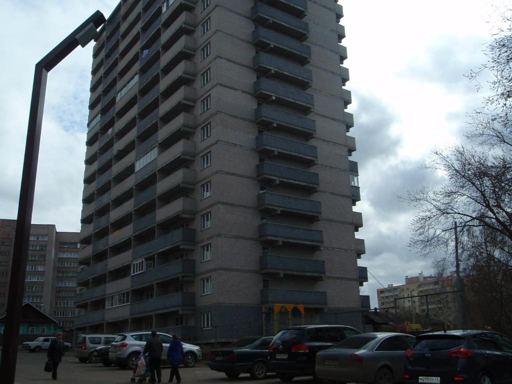 a tall building with cars parked in a parking lot at Apartment on 2-Y Khlynovskiy Pereulok 1 in Kirov
