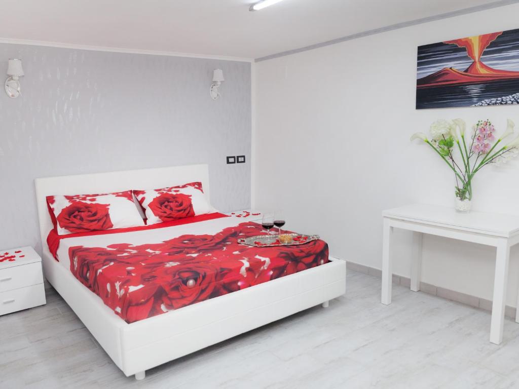 a white bedroom with a bed with red sheets and a table at Short Lets Lulù in Ercolano