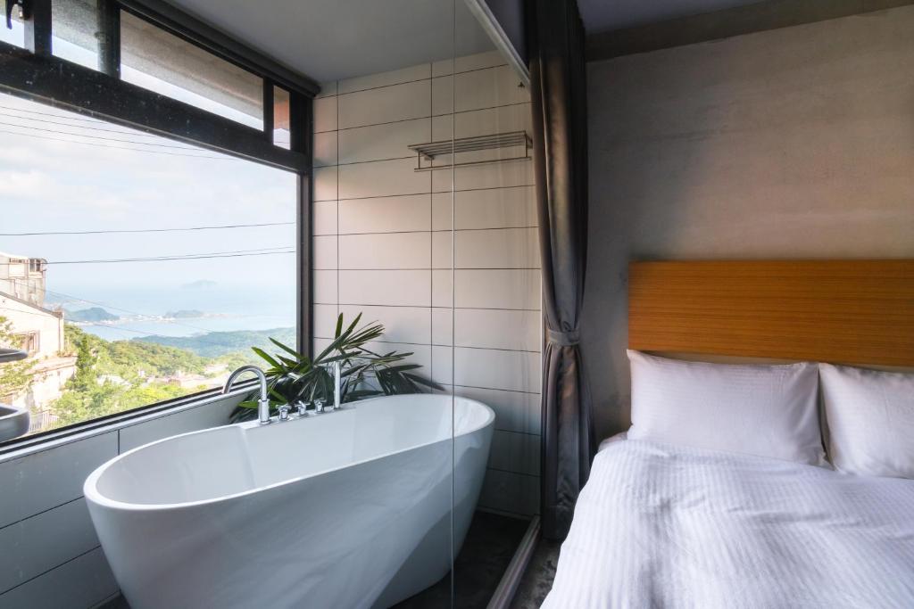 a bathroom with a tub and a bed and a window at H&amp; Jiufen Ore Inn in Jiufen