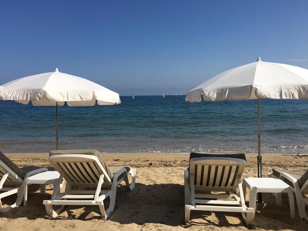 un groupe de chaises et de parasols sur une plage dans l'établissement Jardins du Port Les Issambres - Meublé de Tourisme - Front de mer - Clim, à La Garonnette-Plage