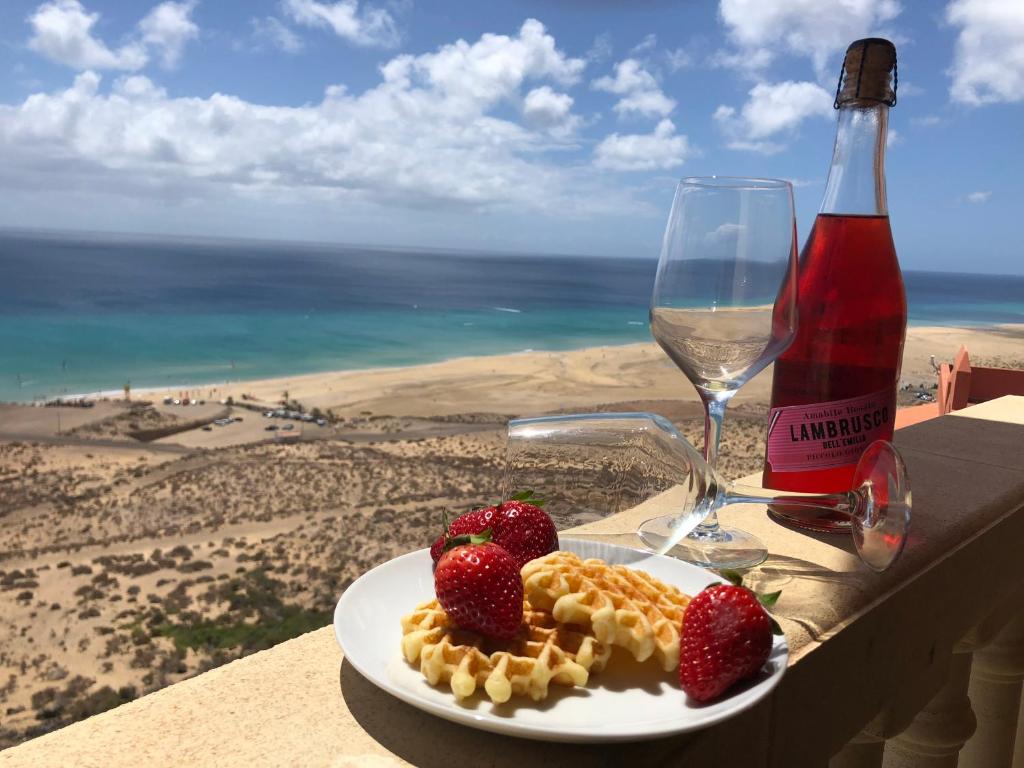 a plate of waffles and strawberries on a table with a bottle of wine at Apart. Playa La Barca in Costa Calma