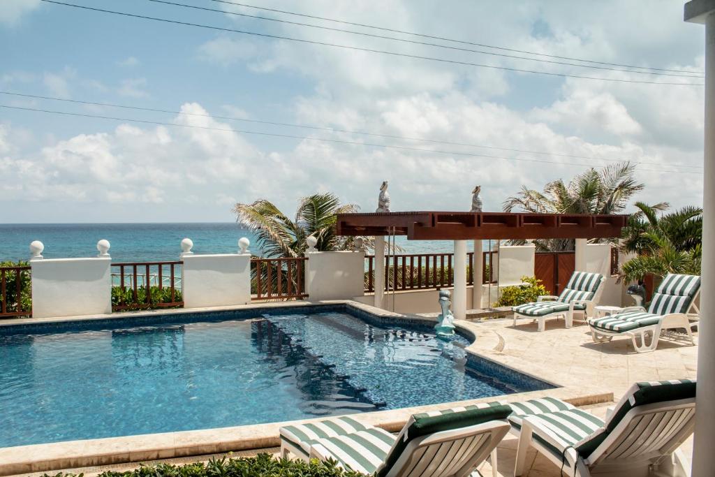 a swimming pool with chairs and the ocean in the background at Villa Isla Dorada in Isla Mujeres