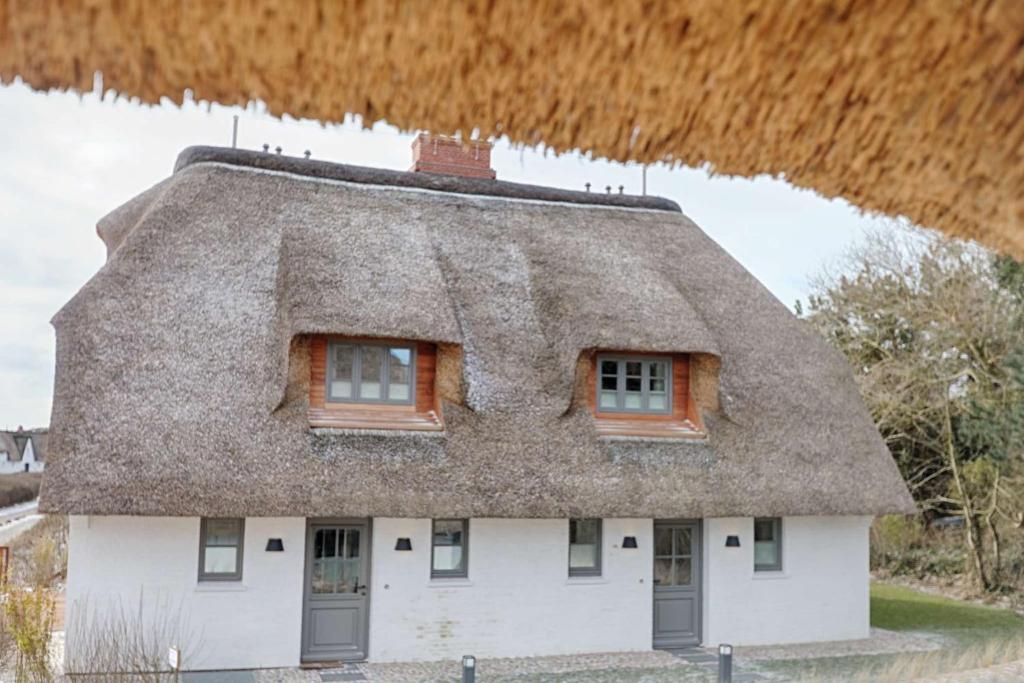 ein Haus mit einem Strohdach und zwei Fenstern in der Unterkunft Rantum Dorf - Ferienappartments im Reetdachhaus 1& 2 in Rantum