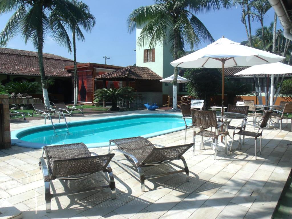 - une piscine avec des chaises, des tables et un parasol dans l'établissement Apart Hotel Guaiúba, à Guarujá