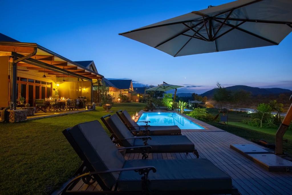 un patio trasero con piscina, sillas y sombrilla en Kambaku River Lodge, en Malelane
