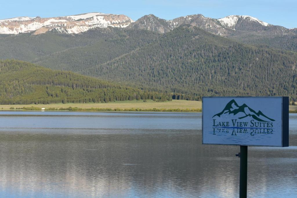 um sinal em frente a um lago com montanhas em Lake View Suites em West Yellowstone