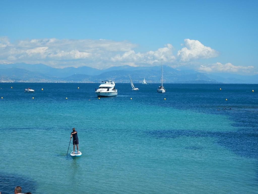 a man on a paddle board in the water with boats at Hotel Miramar- Cap d'Antibes - La Garoupe plage in Antibes