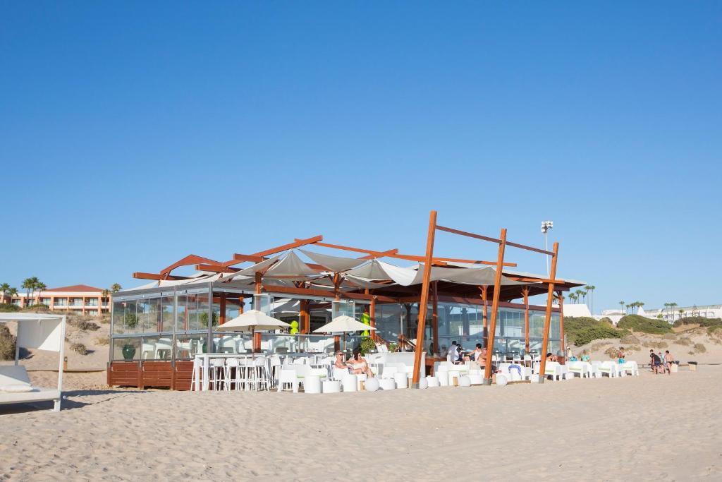 a restaurant on the beach with chairs and umbrellas at Hipotels Barrosa Park in Chiclana de la Frontera