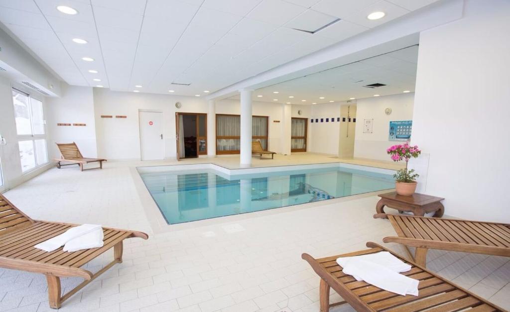 a swimming pool in a building with benches and chairs at Les Gentianes - Cimes et Neige in Puy-Saint-Vincent