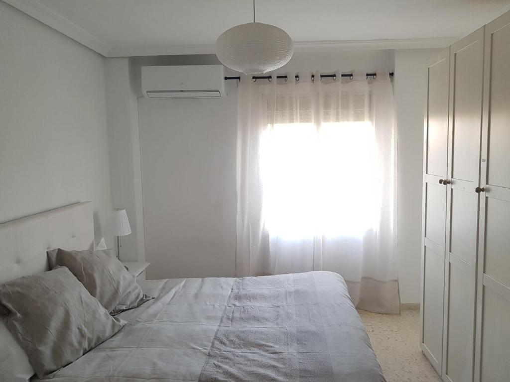 Habitación blanca con cama y ventana en Luminoso y amplio apartamento, en Sevilla