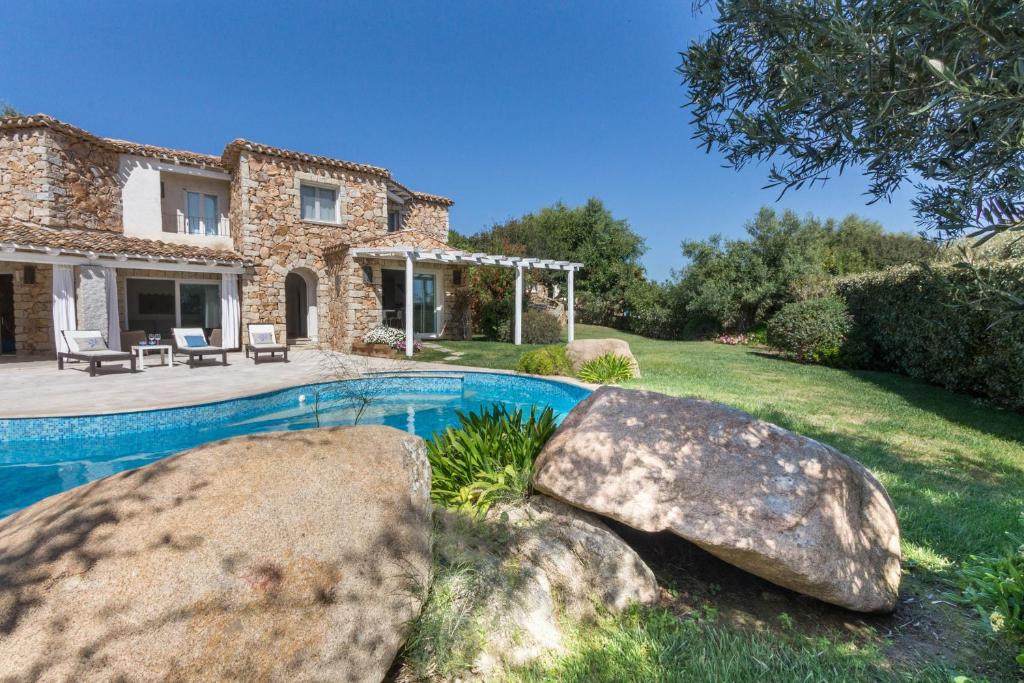 une maison en pierre avec une piscine et deux grands rochers dans l'établissement Villa Ginestra con piscina e giardino privato a 500 mt dal mare, à Castiadas