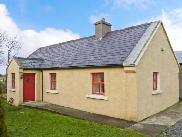 una pequeña casa amarilla con puerta roja en Cavan Hill Cottage, en Ballinrobe