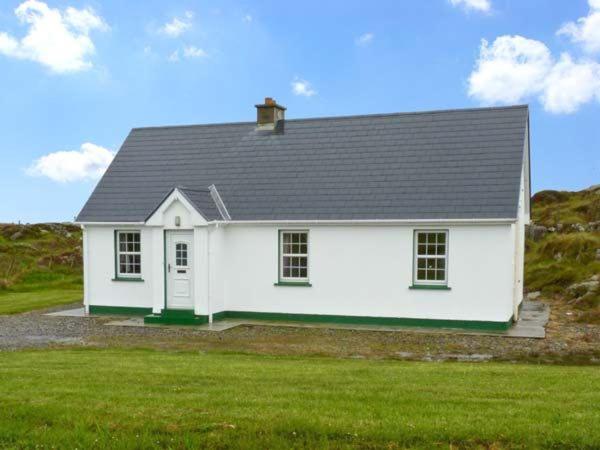 une maison blanche avec un toit noir sur un champ vert dans l'établissement Lully More Cottage, à Doochary